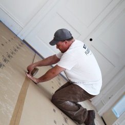 A man leaning on the floor while connecting two protective floor surfaces with flooring seam tape