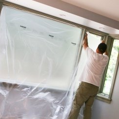 A man covering a window with self-adhering plastic sheeting
