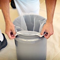 A man's hands adding a paint strainer bag to an empty paint pot