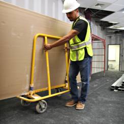 A construction worker moving a tack back protective surface in a dolly car.